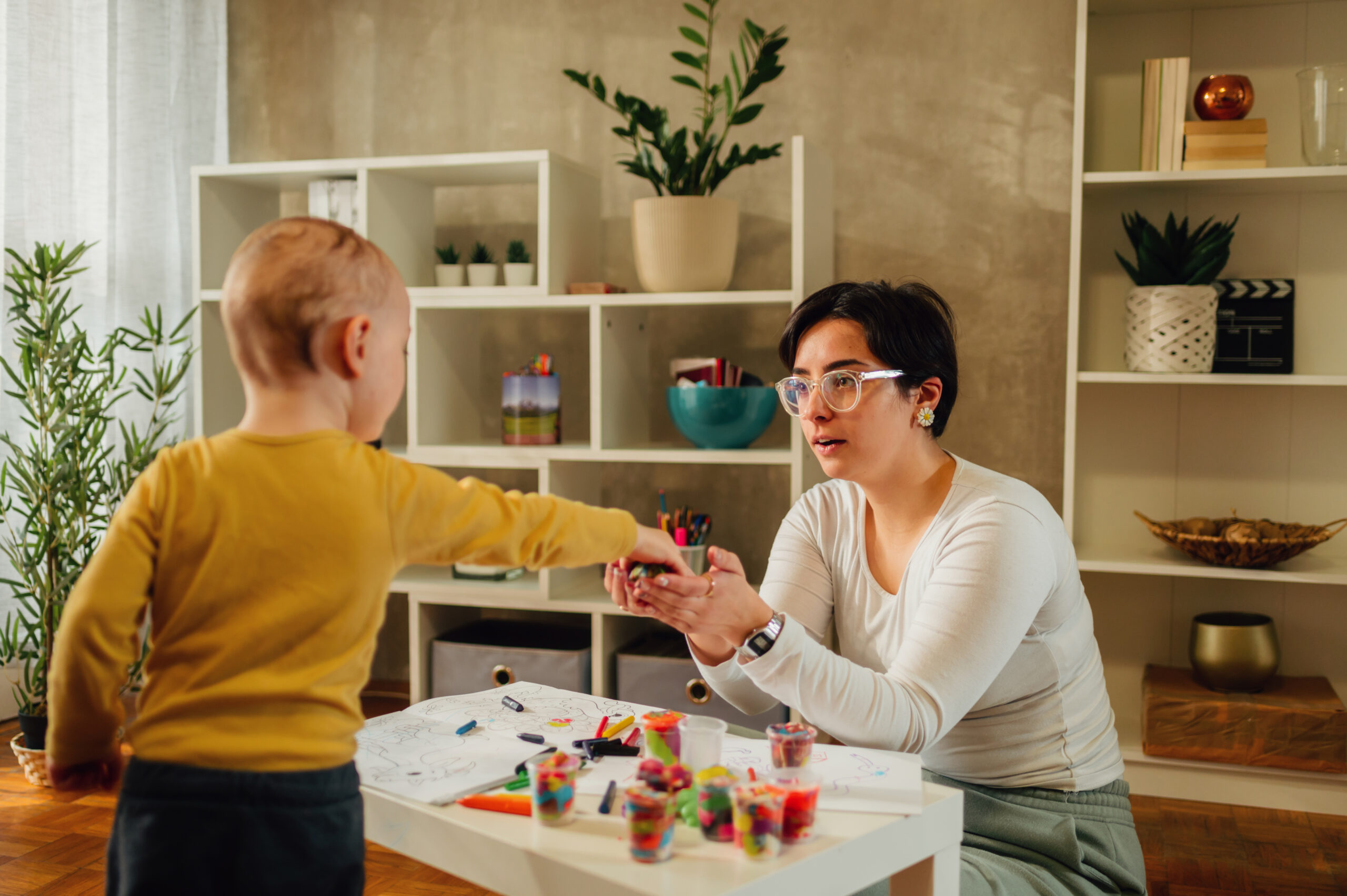 Family of two improving fine motor skill trough the games while playing at home with toys and crayons. Toddler boy playing with his mother or aunt. Funny educational games for children concept.